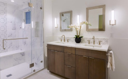 Bathroom of a San Francisco home with a glass door to a seated marble shower, wood and stone vanity, modern lighting and a blooming orchid between two sinks. 