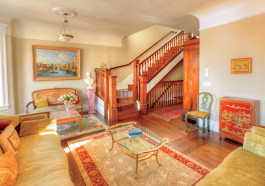 Exquisite San Francisco residence, living room with marble statues on pedestals, museum art on the walls, velvet couches, high vaulted ceilings, a wooden staircase with intricate detailing which leads to the upper and lower floors, and natural late-afternoon light filling the room. 